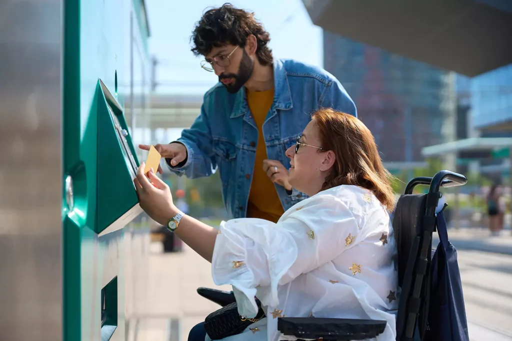 Disabled woman in wheelchair with support worker paying for travel card